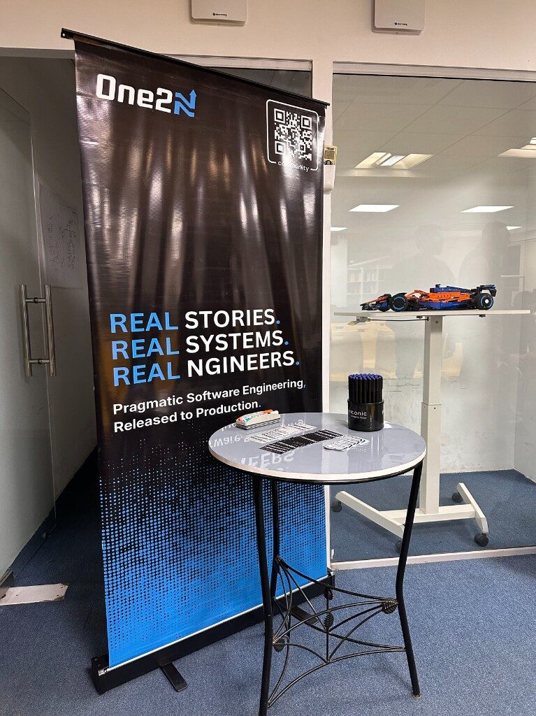 One2N banner - Real stories, real systems, real engineers - with promo table and model car, Episode 2